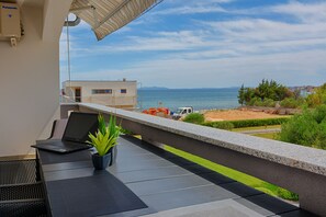 A balcony with a laptop, a potted plant, and a view of the sea and distant buildings. - Apartments Basic (Vir)
