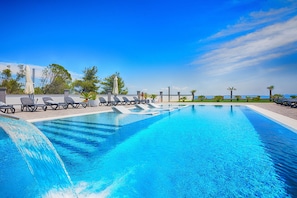 A swimming pool with lounge chairs and a waterfall feature. - Apartments Basic (Vir)