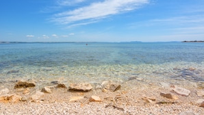 A clear view of a pebble beach with calm water and distant land. - Apartments Basic (Vir)