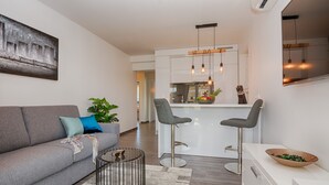 A modern living room with a grey sofa, a coffee table, and a bar area with two stools. - Apartments Basic (Vir)