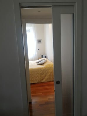Ein Schlafzimmer mit einem Bett, Holzboden und einer Tür zu einem anderen Raum.