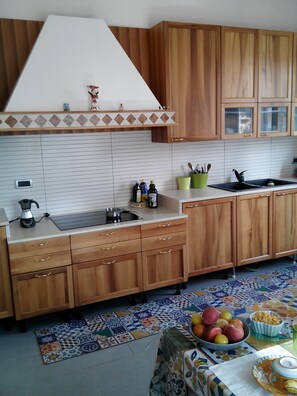 Eine Küche mit Holzschränken, einer gefliesten Spritzschutzwand und einer Arbeitsplatte mit Wasserkocher und Flaschen.