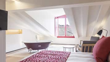 Un dormitorio con tragaluces, una bañera, una cama, una mesita y una silla.