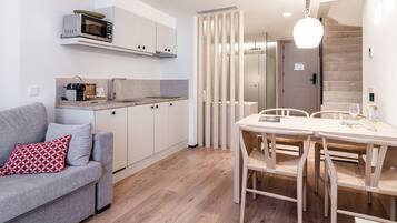 Een knus woongedeelte met een kitchenette, een eethoek en een bank met een kussen met een rood patroon.