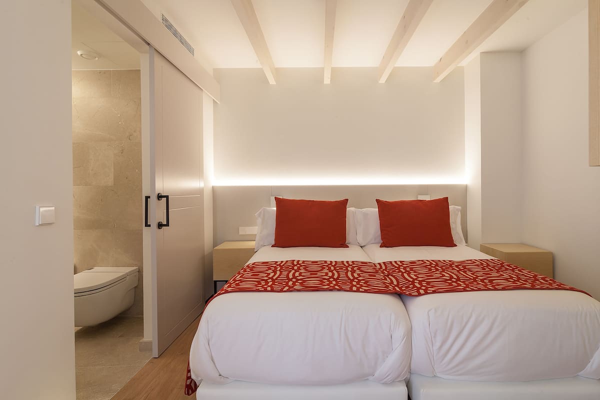 Ein modernes Schlafzimmer mit einem großen Bett, zwei Nachttischen und einer roten, gemusterten Decke.