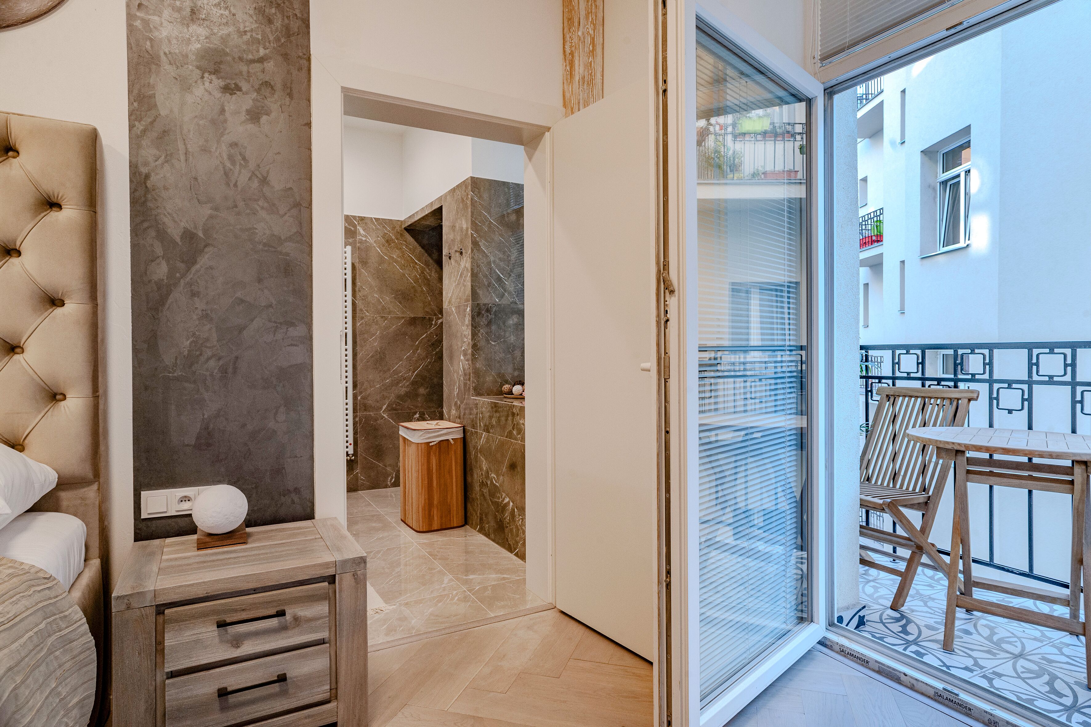 Une chambre à coucher moderne avec une tête de lit capitonnée, une table de chevet dotée de tiroirs et un mur d’accent en marbre.