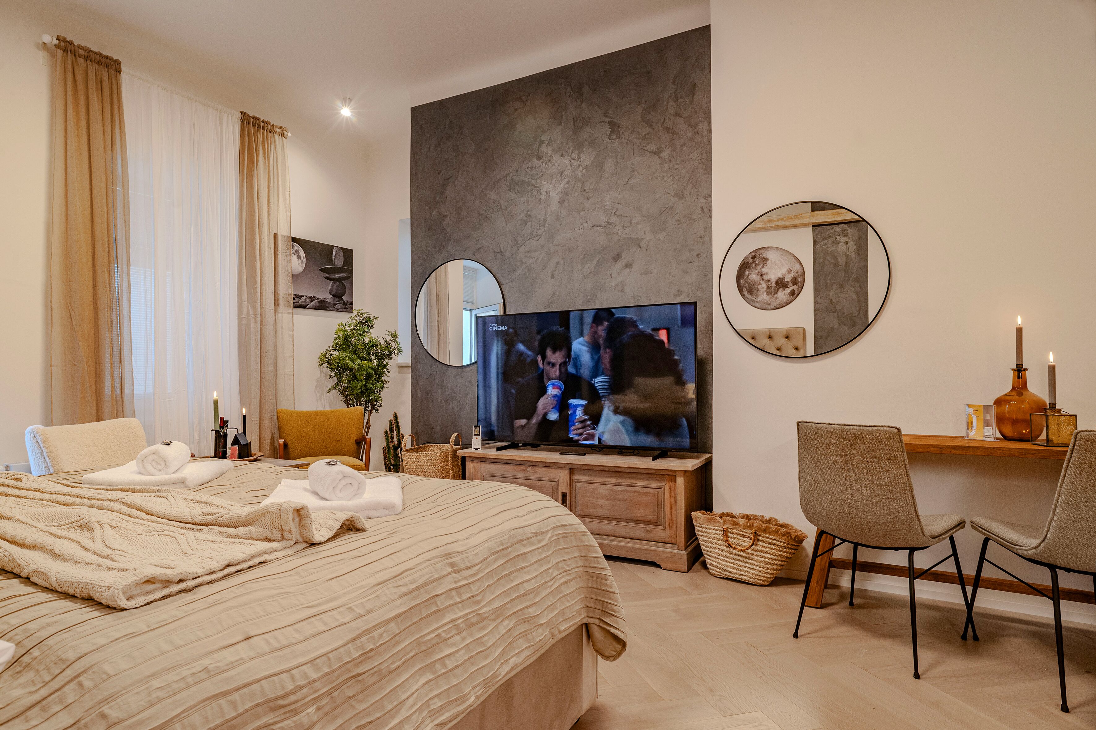 A hotel room with a large bed, a TV, a desk with a chair, and a wall-mounted mirror.