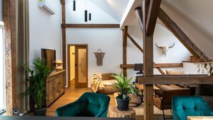 Un loft espacioso con vigas de madera a la vista, un techo alto y una zona de estar acogedora con sillas color turquesa y una mesa de madera.