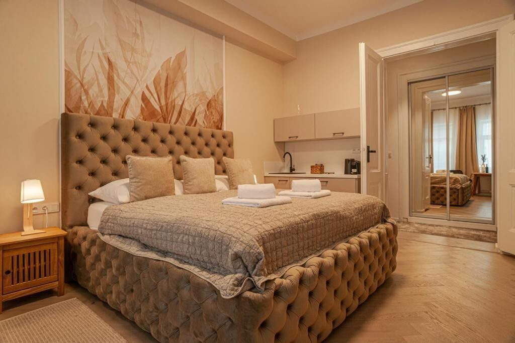 A bedroom with a tufted headboard, a bed with a quilt, a nightstand with a lamp, and a view into the adjacent bathroom.