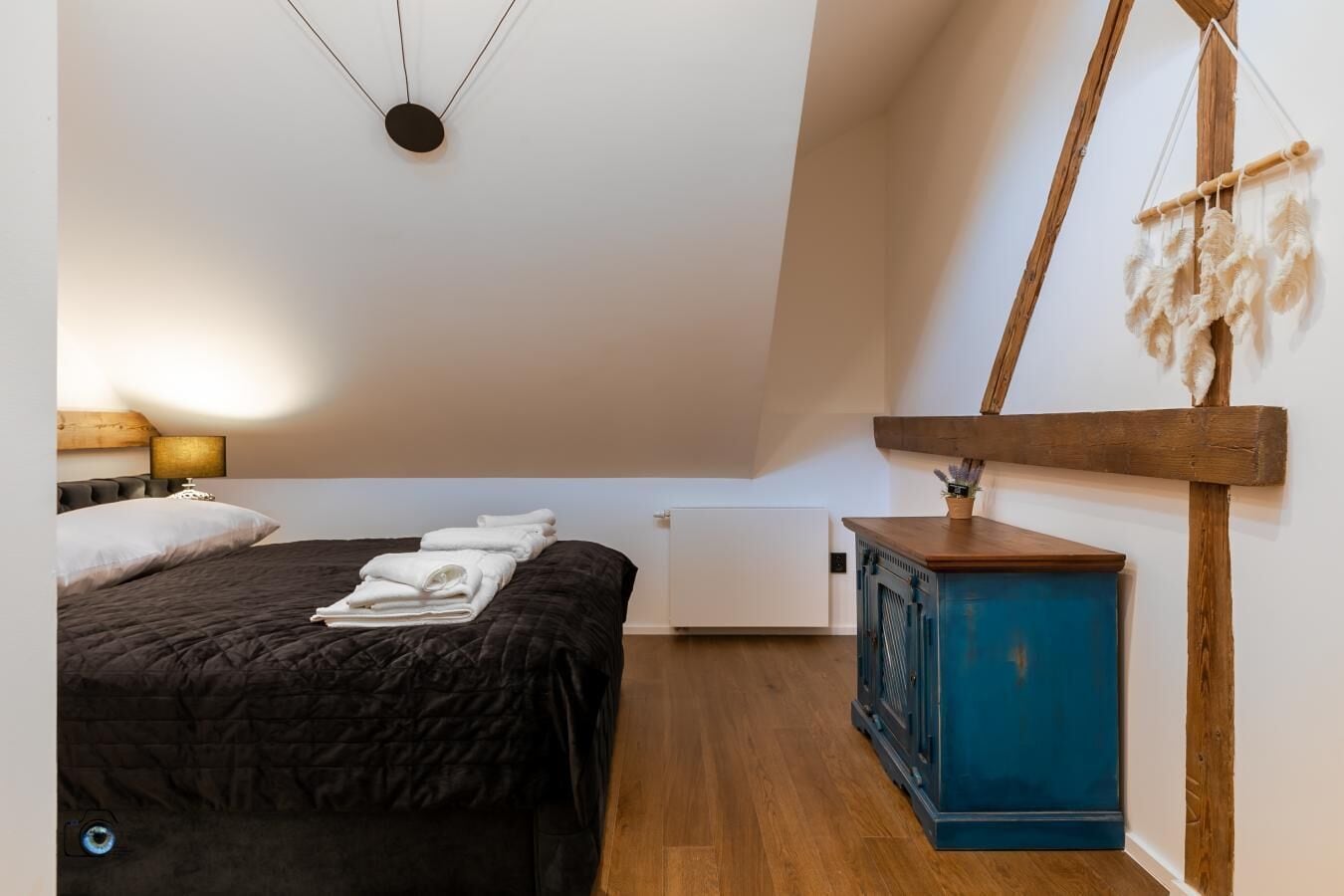 A bedroom with a bed, a nightstand, a dresser, and a wall-mounted macrame piece.