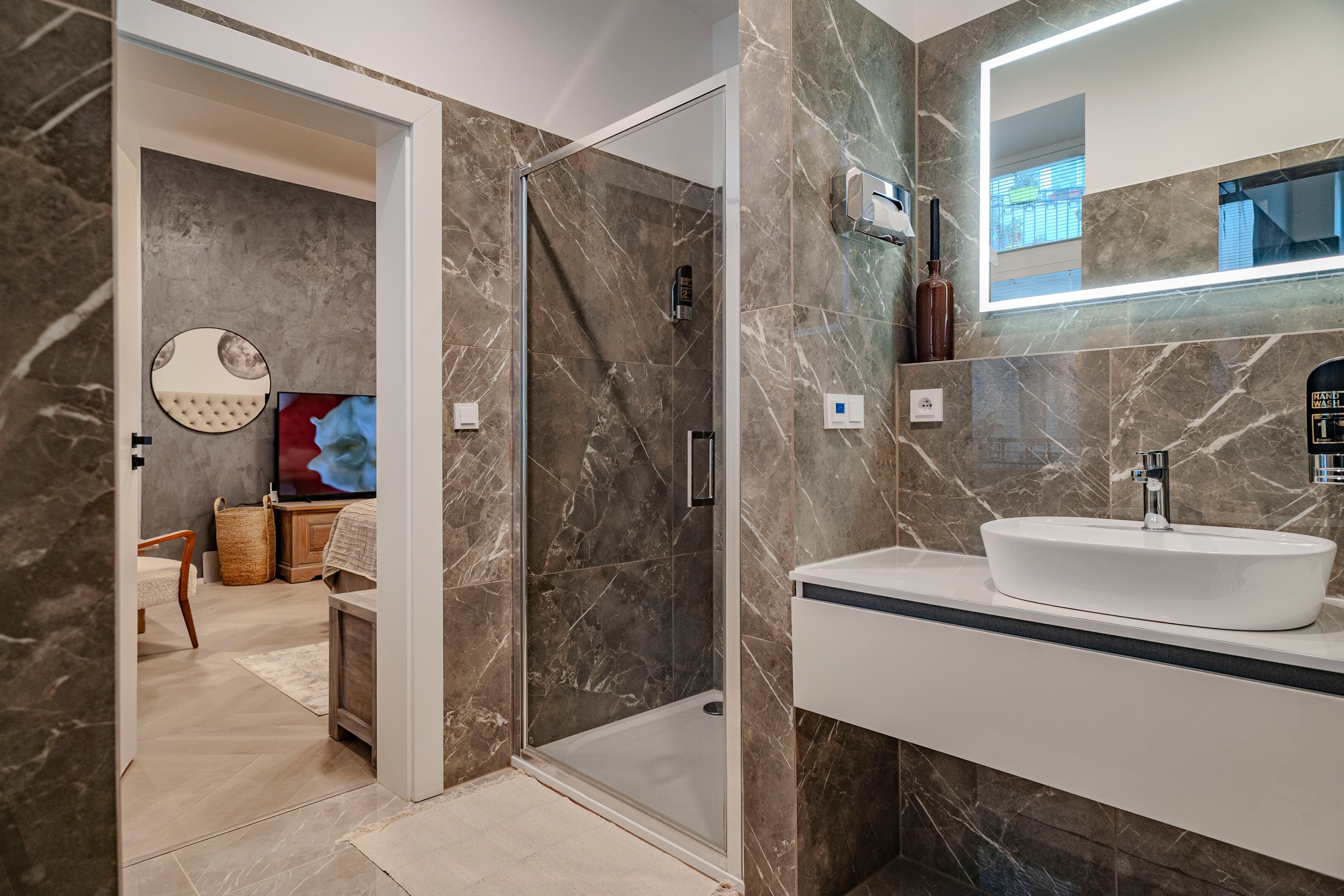 A modern bathroom with a glass-enclosed shower, a white sink, and a large mirror.