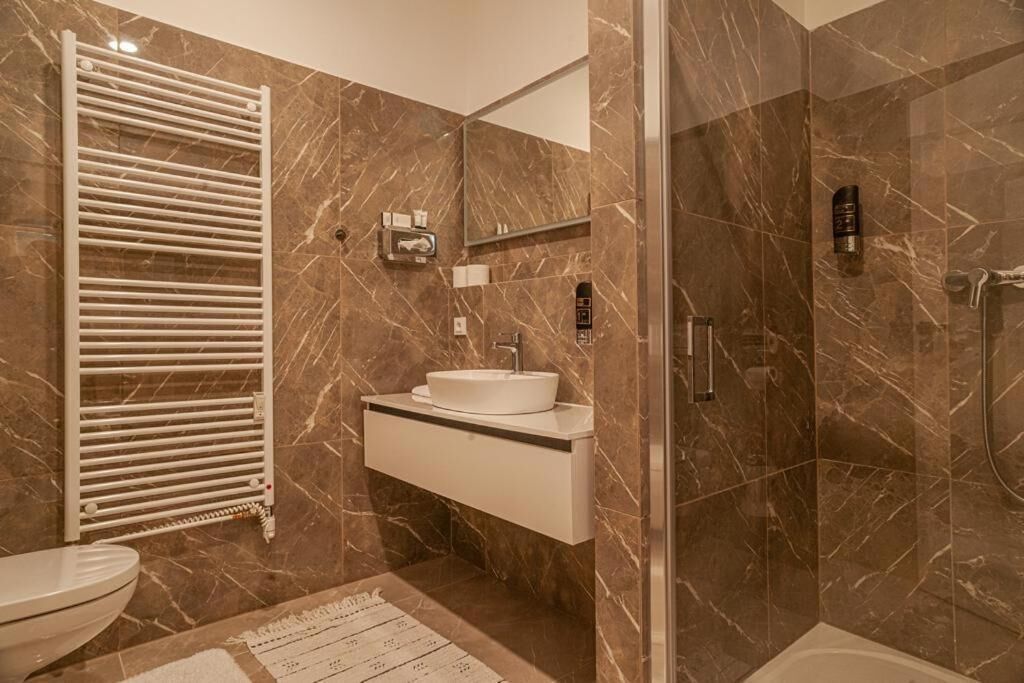 Un baño moderno con suelo de mármol, lavamanos blanco, cabina de ducha de vidrio y un perchero para toallas.