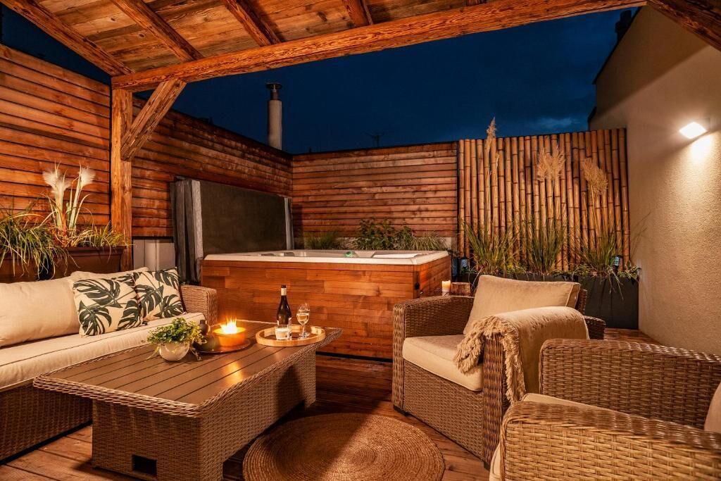 A cozy outdoor patio with wicker furniture, a hot tub, and ambient lighting.