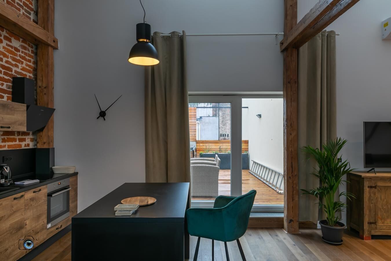 A modern kitchen with a dining area, a TV, and a balcony with outdoor seating.