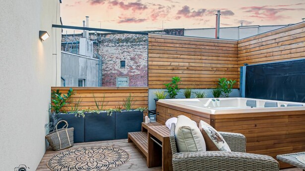 Una terraza en la azotea con jacuzzi, mobiliario de mimbre y plantas en macetas.