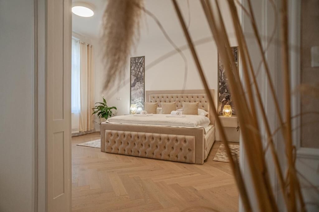 A bedroom with a large bed, a bedside table with a lamp, and a potted plant.