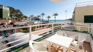 A balcony with a white table and chairs, overlooking a beach with palm trees and a clear sky. - Neighbours Apartments (Calvia)