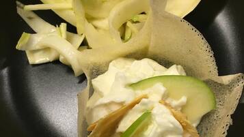 A black plate with a crepe topped with cream cheese, cucumber slices, and a green leaf.