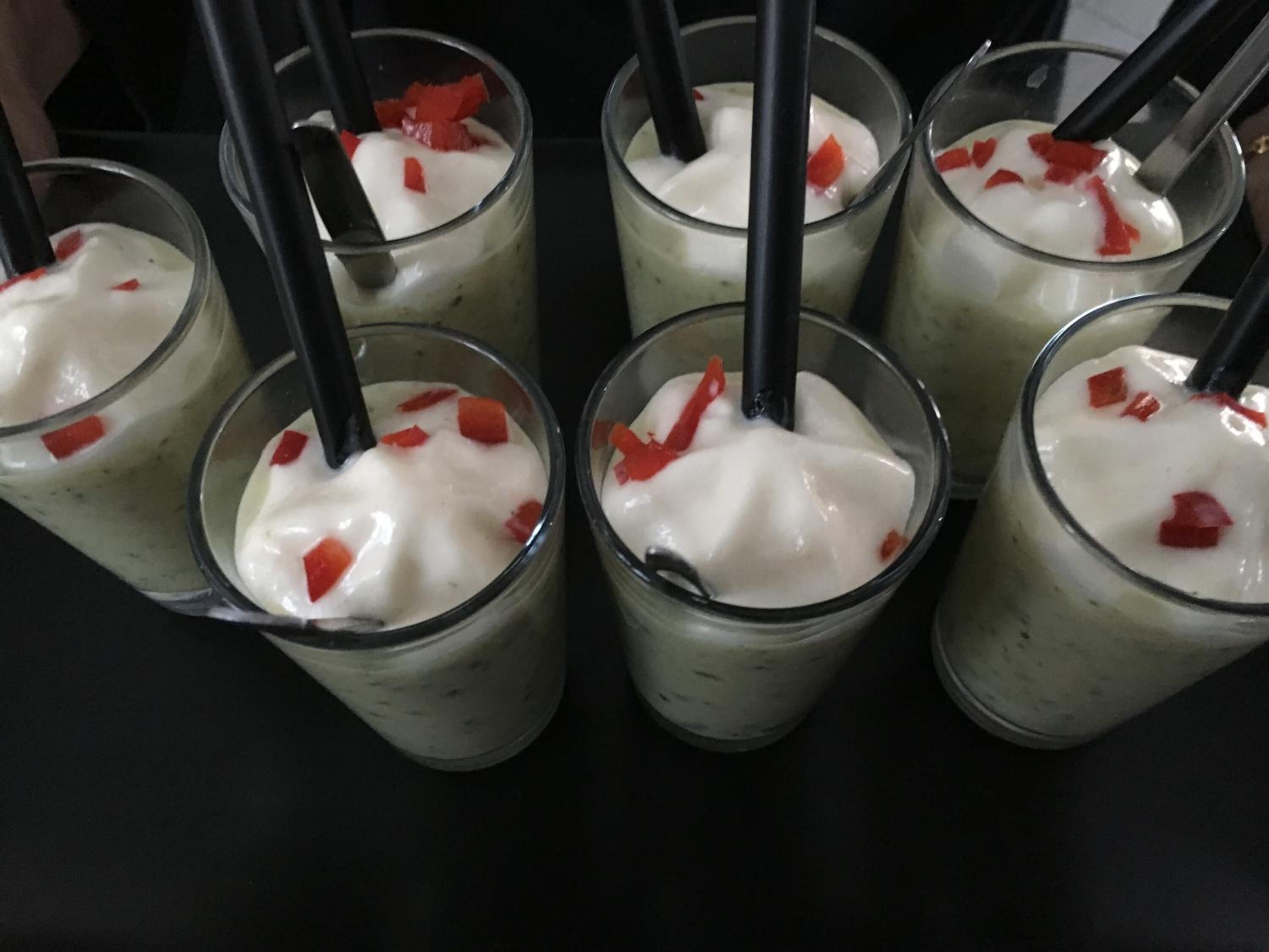 Six glasses of a white beverage with red fruit pieces and black straws.