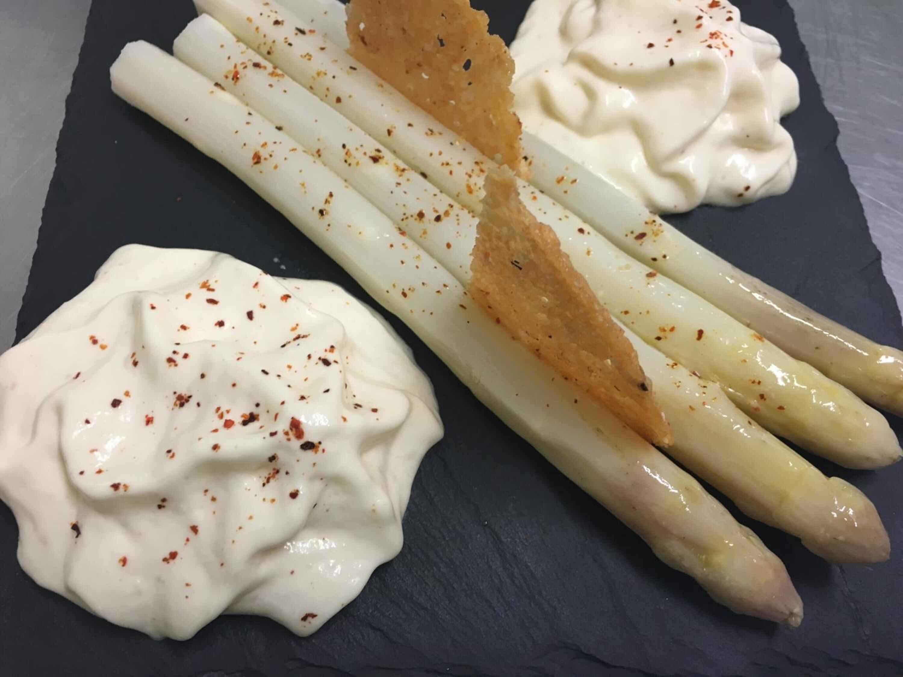 A plate with asparagus and two dollops of creamy sauce, possibly hollandaise, garnished with red pepper flakes.