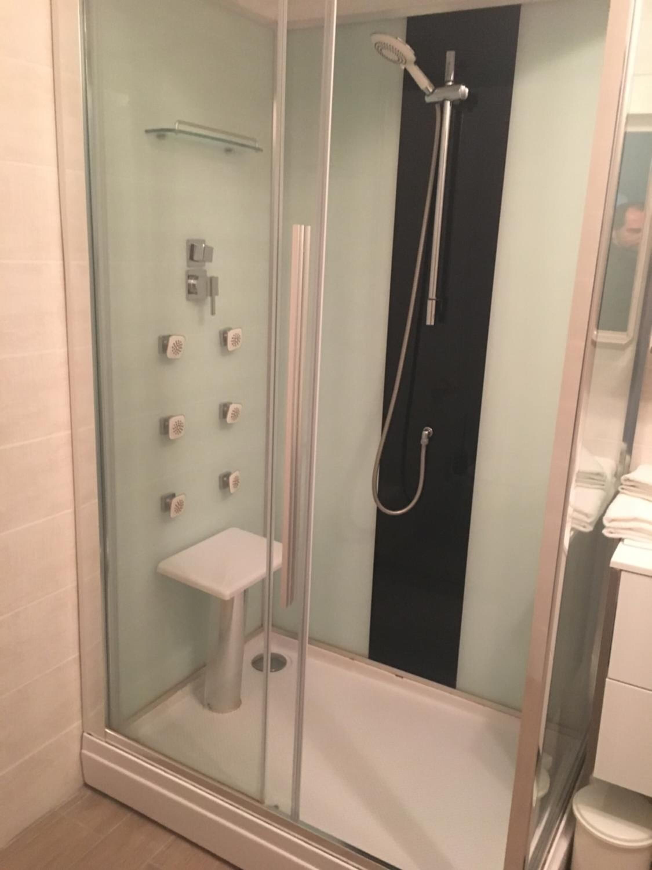 Un box de ducha con paredes de vidrio, un grifo pequeño blanco y un perchero para toallas.
