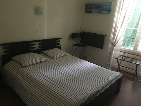 Un dormitorio con cama, una silla, un escritorio y un cuadro en la pared.
