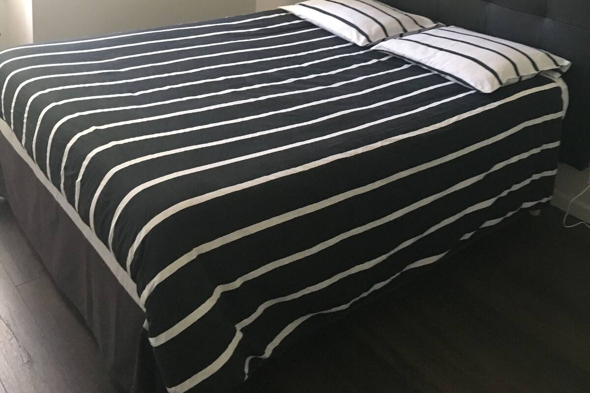 A bed with a striped bedspread, a dark headboard, and a small bedside table with a lamp.
