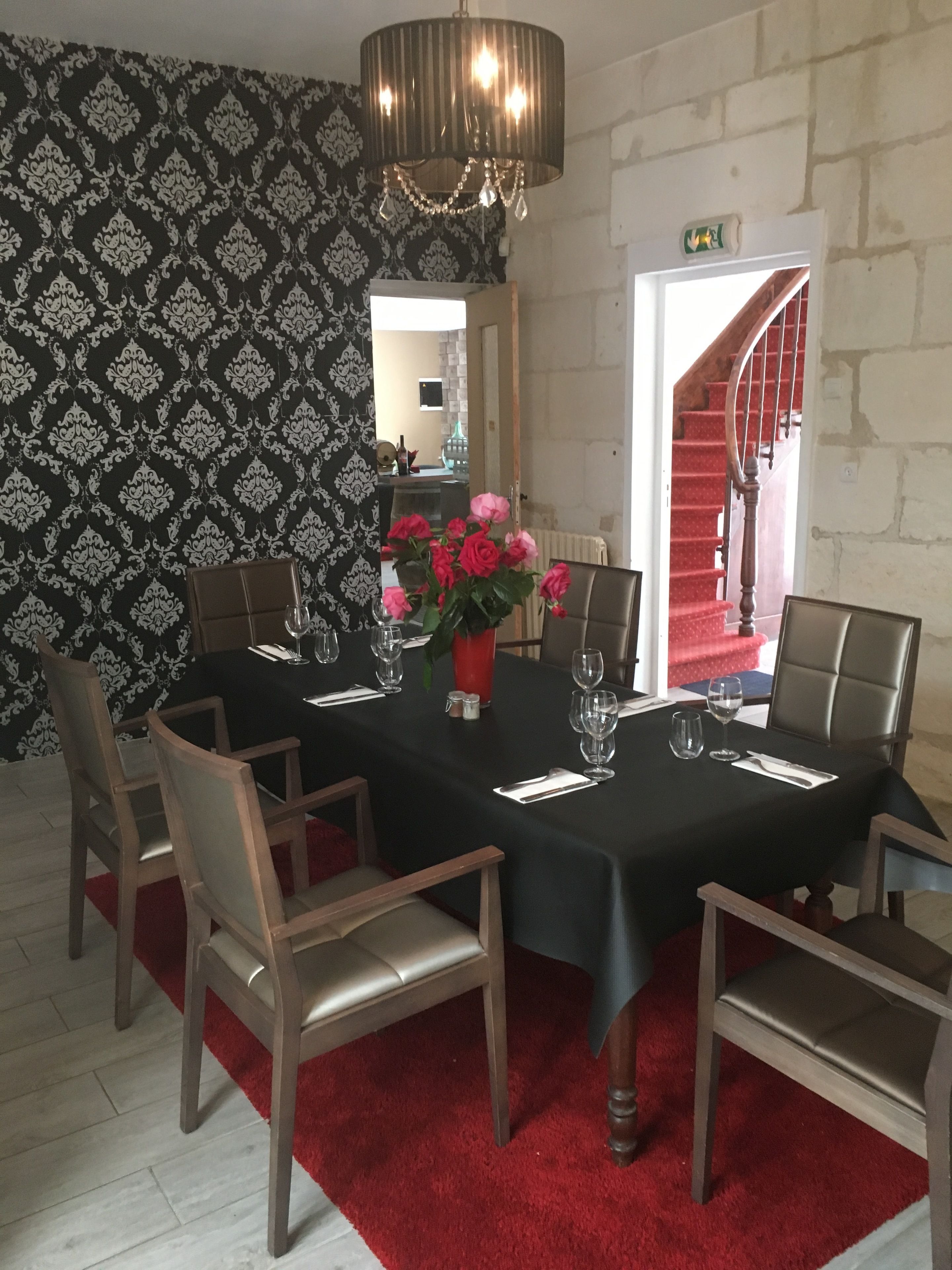Un comedor con mantel negro, seis sillas de madera, un jarrón con flores rosas y una araña.