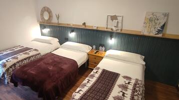A hotel room with three beds, a wooden nightstand, a mirror, and wall-mounted lights.