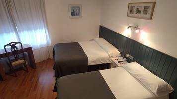 Habitación de hotel con dos camas, un escritorio, una silla y una mesita de noche con lámpara y teléfono.