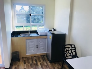 Cocina compacta con ventana, pileta, alacenas, refrigerador y una silla.