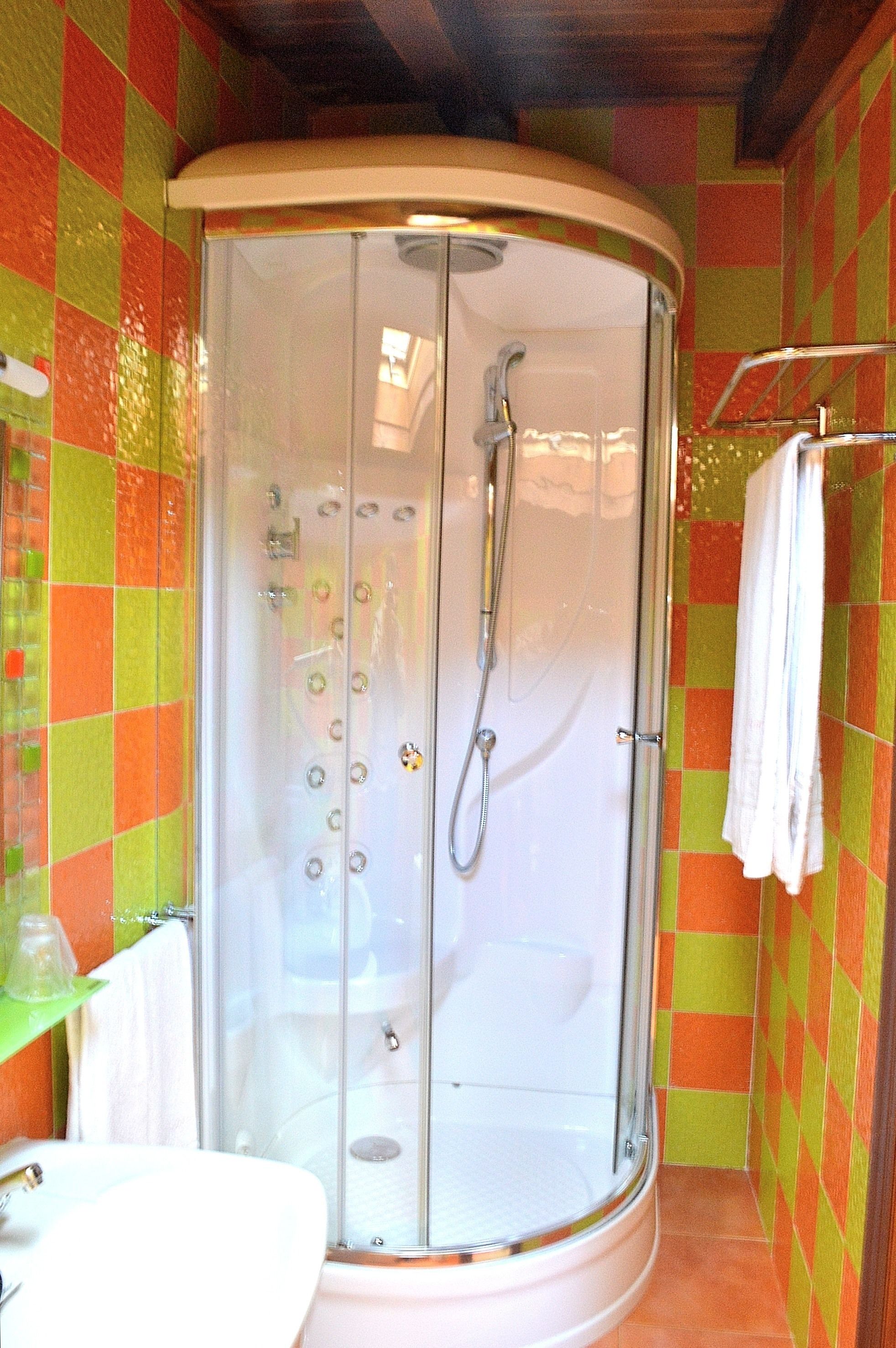 Ducha con puerta de vidrio, lavamanos blanco y toallero.