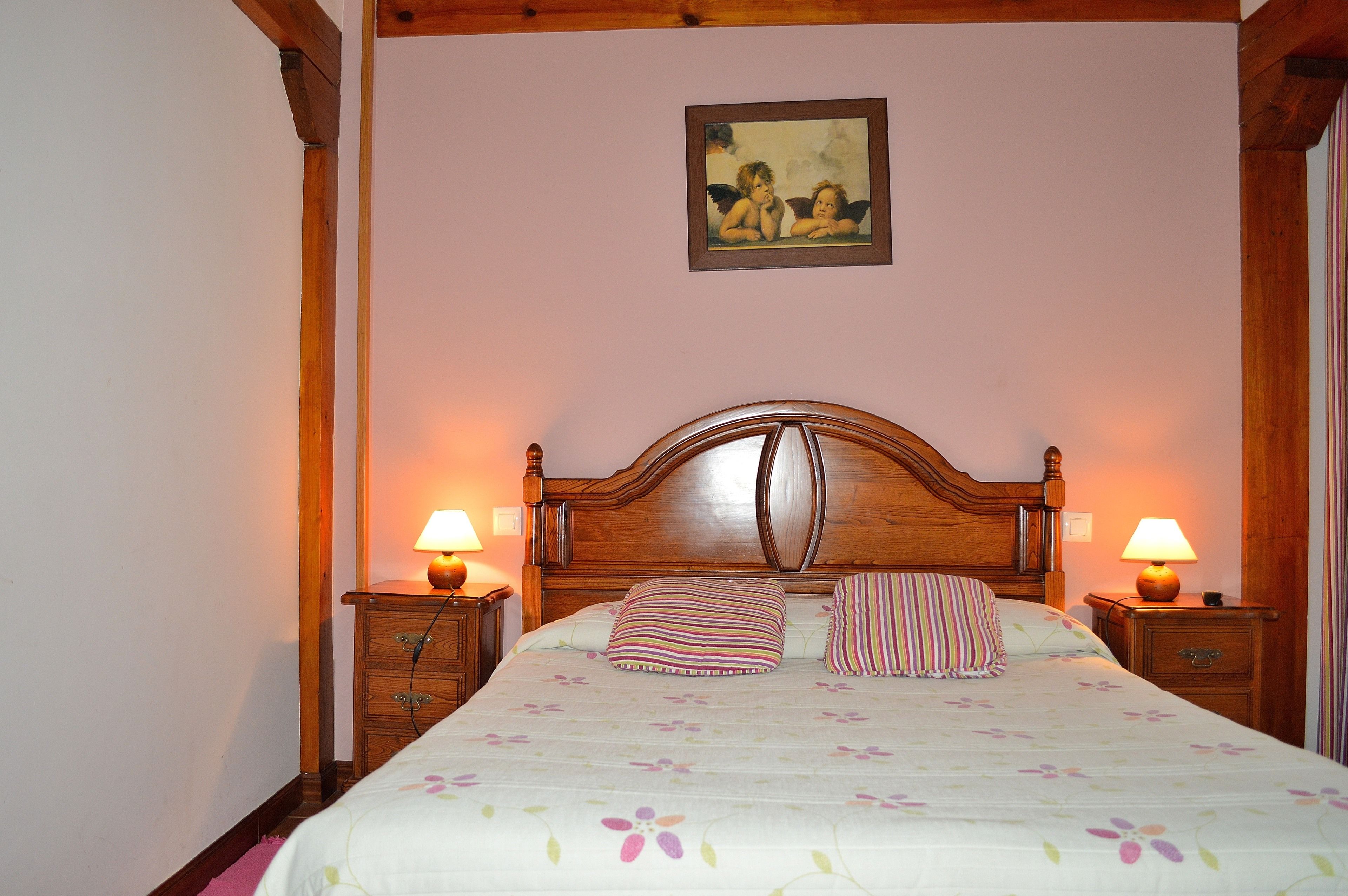 Ein Schlafzimmer mit einem Holzkopfende, zwei Nachttischen mit Lampen, einer blumigen Bettdecke und einem gerahmten Bild an der Wand.