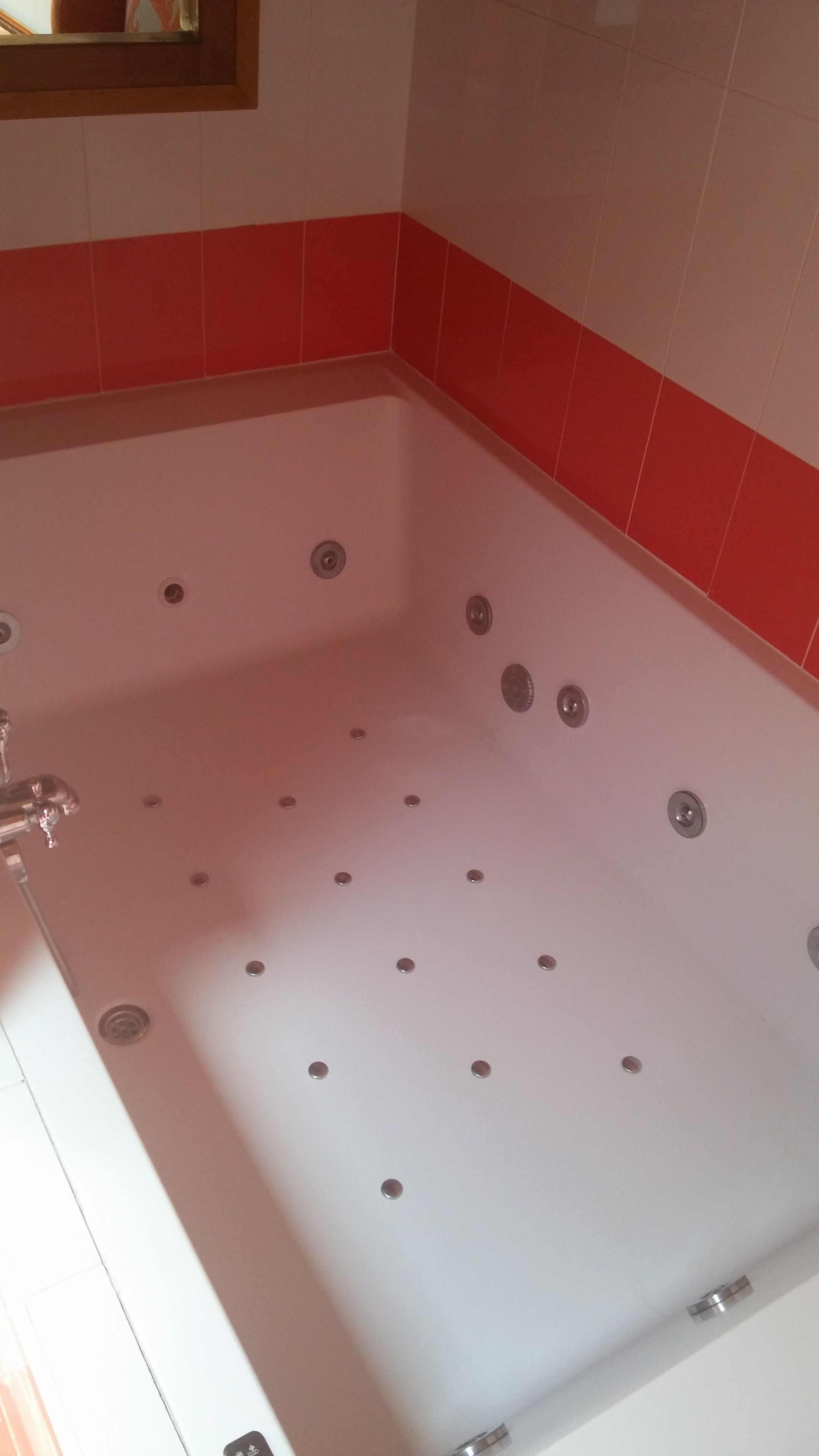 A bathroom with a large bathtub, red and white tiled walls, and a mirror above the tub.