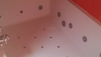A bathroom with a large bathtub, red and white tiled walls, and a mirror above the tub.