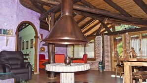 Ein rustikales Interieur mit großem Kupferofen, Holzbalken, einem runden Tisch und einem Ledersessel.