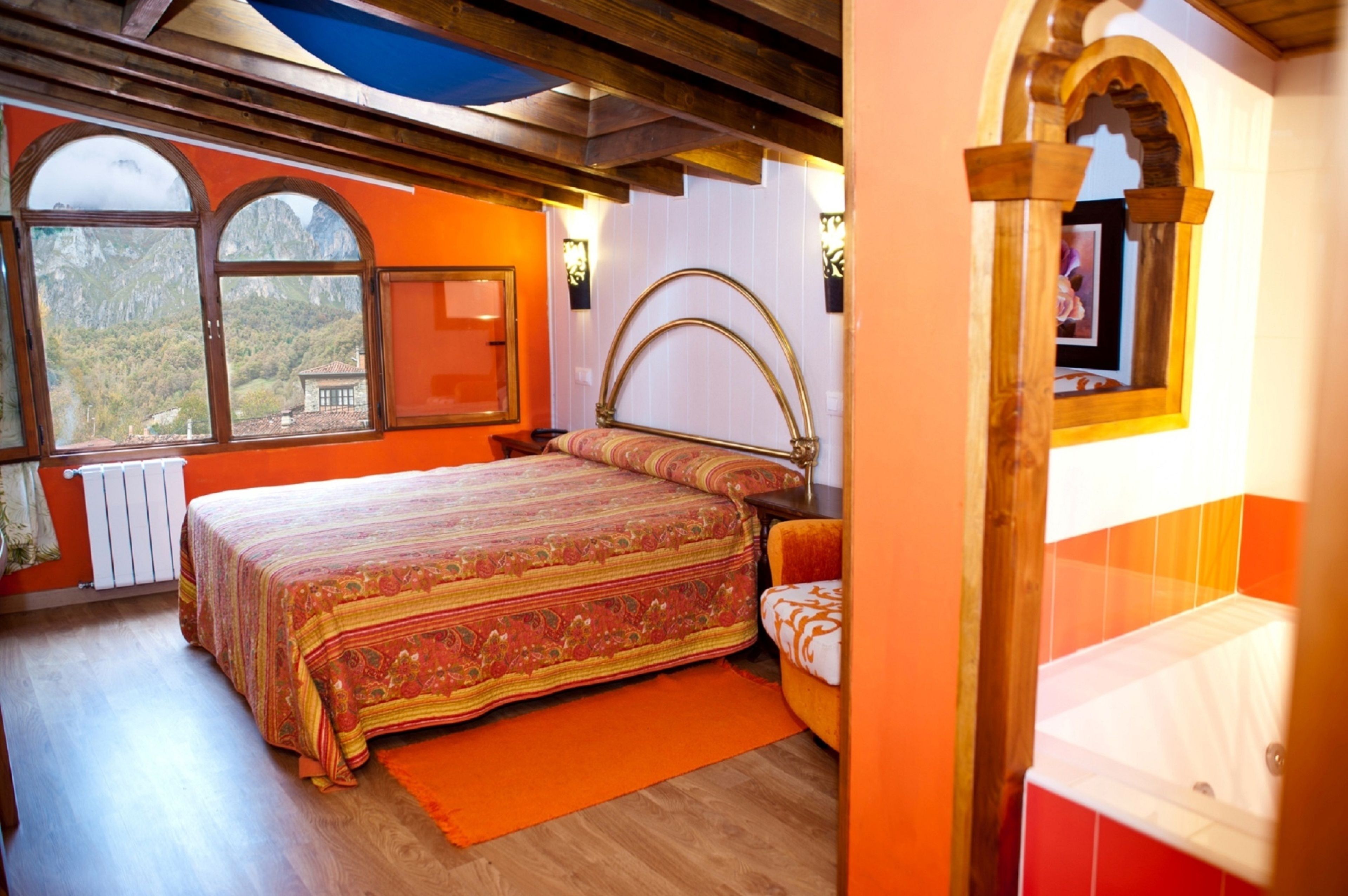 Une chambre avec un grand lit, une tête de lit en bois, une vue sur les montagnes par la fenêtre et un plafond en bois.