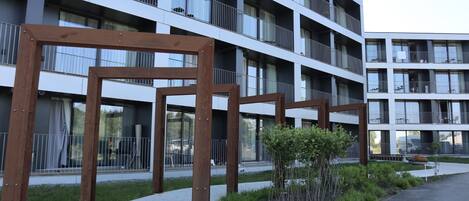 A modern multi-story building with balconies, a paved walkway, and a small garden area.