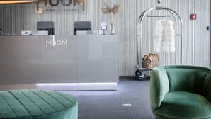A reception area with a modern design, featuring a reception desk, two chairs, a green ottoman, and a hanging fur coat. - Hoom Home & Hotel (Jarfalla)