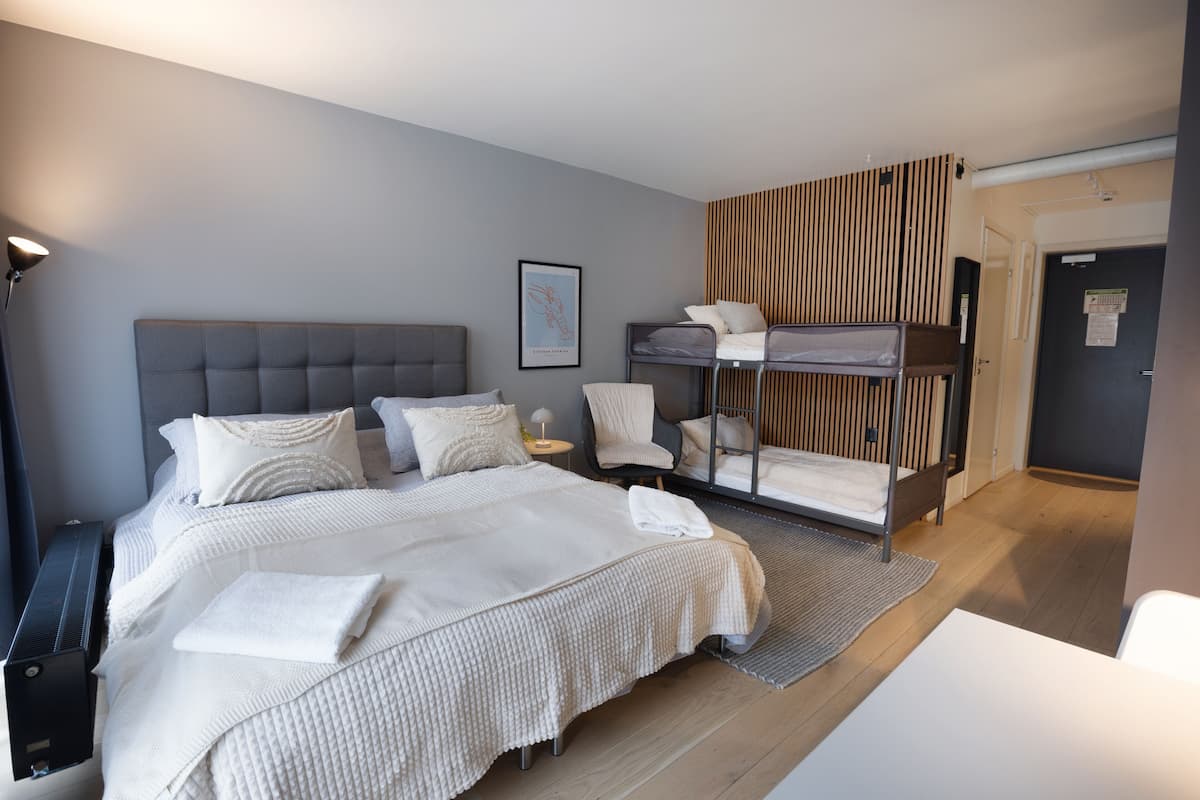 A modern hotel room with a large bed, a bunk bed, a desk, and a chair.