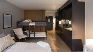 A modern hotel room with a bunk bed, a desk, a chair, and a kitchenette. - Hoom Home & Hotel (Jarfalla)