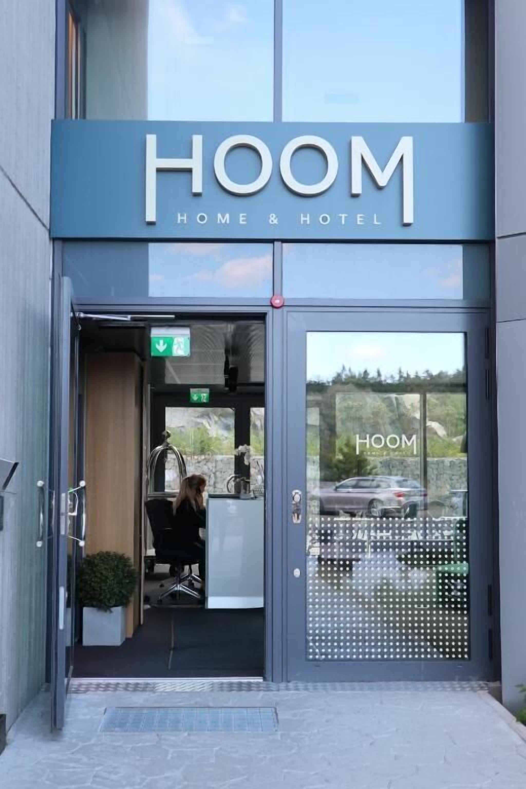 Um edifício moderno com entrada de vidro e a inscrição 'HOOM HOME & HOTEL' em destaque.