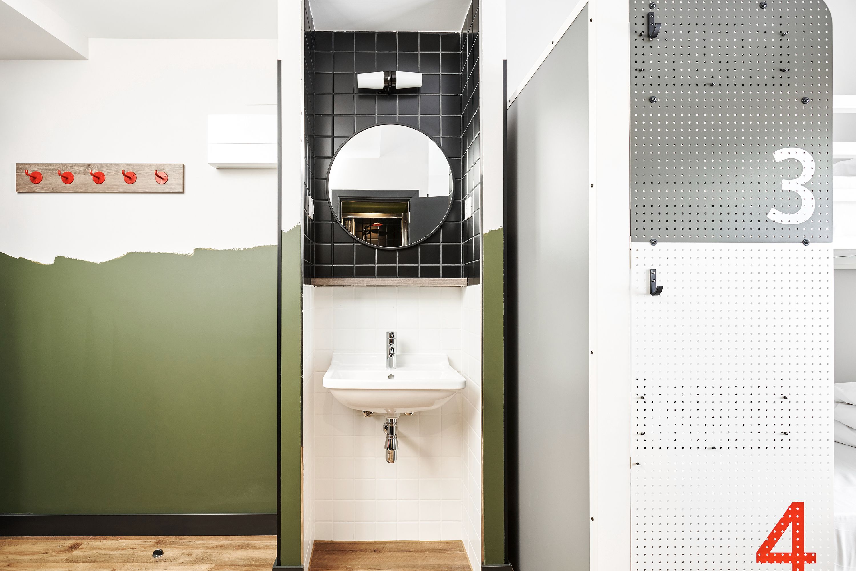 Ein Badezimmer mit einem weißen Waschbecken, einem Spiegel und einer grünen Wand. Ein Holzboden und eine Metallwandverkleidung mit Zahlen sind ebenfalls vorhanden.