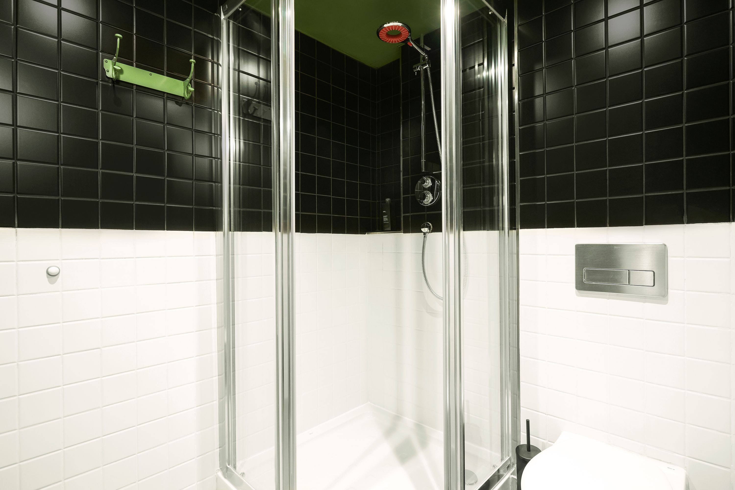A shower with a glass door, a green towel rack, and a white toilet in a bathroom with black and white tiled walls.