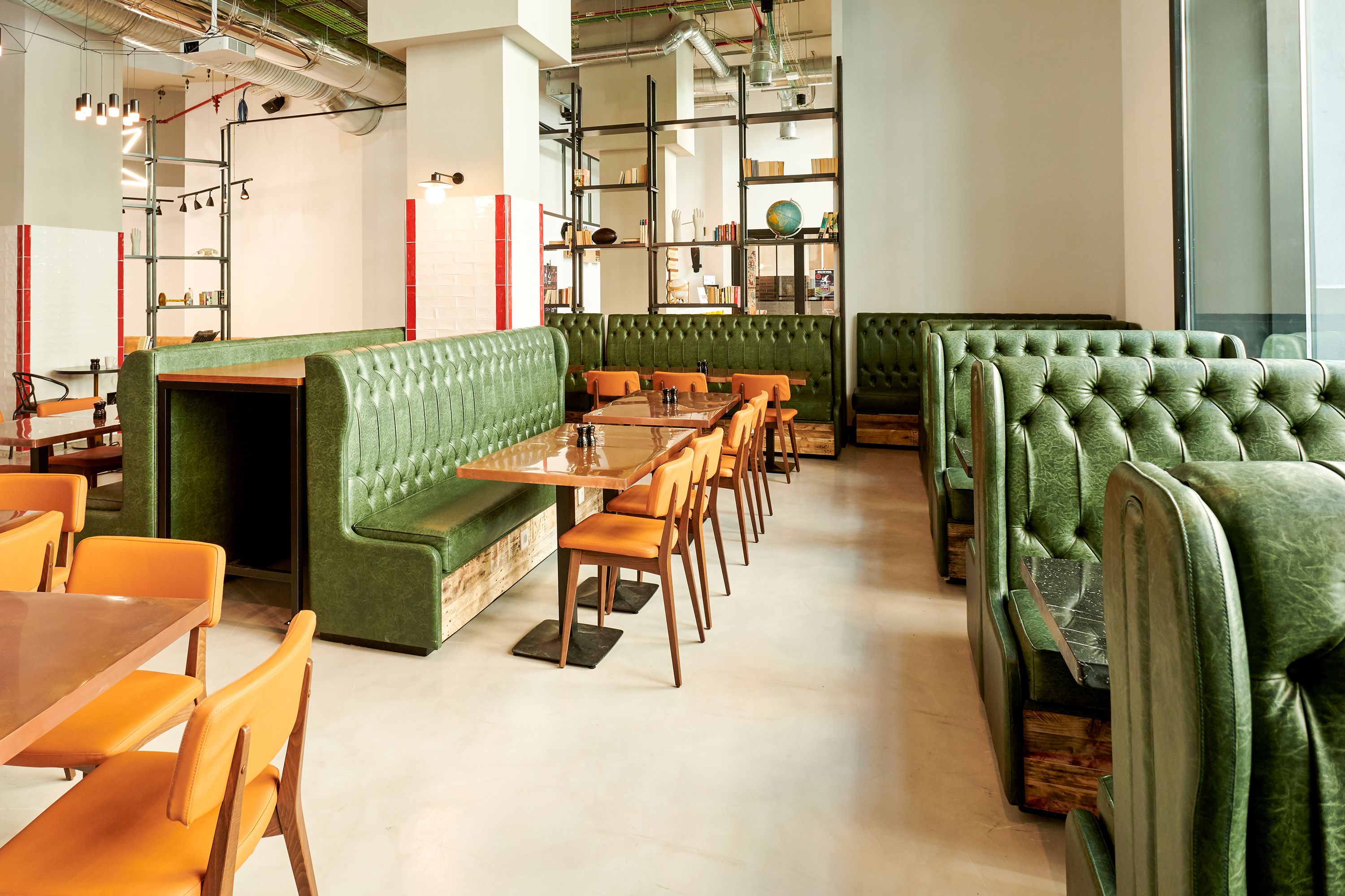 A restaurant interior with green upholstered booths, wooden tables, and orange chairs.