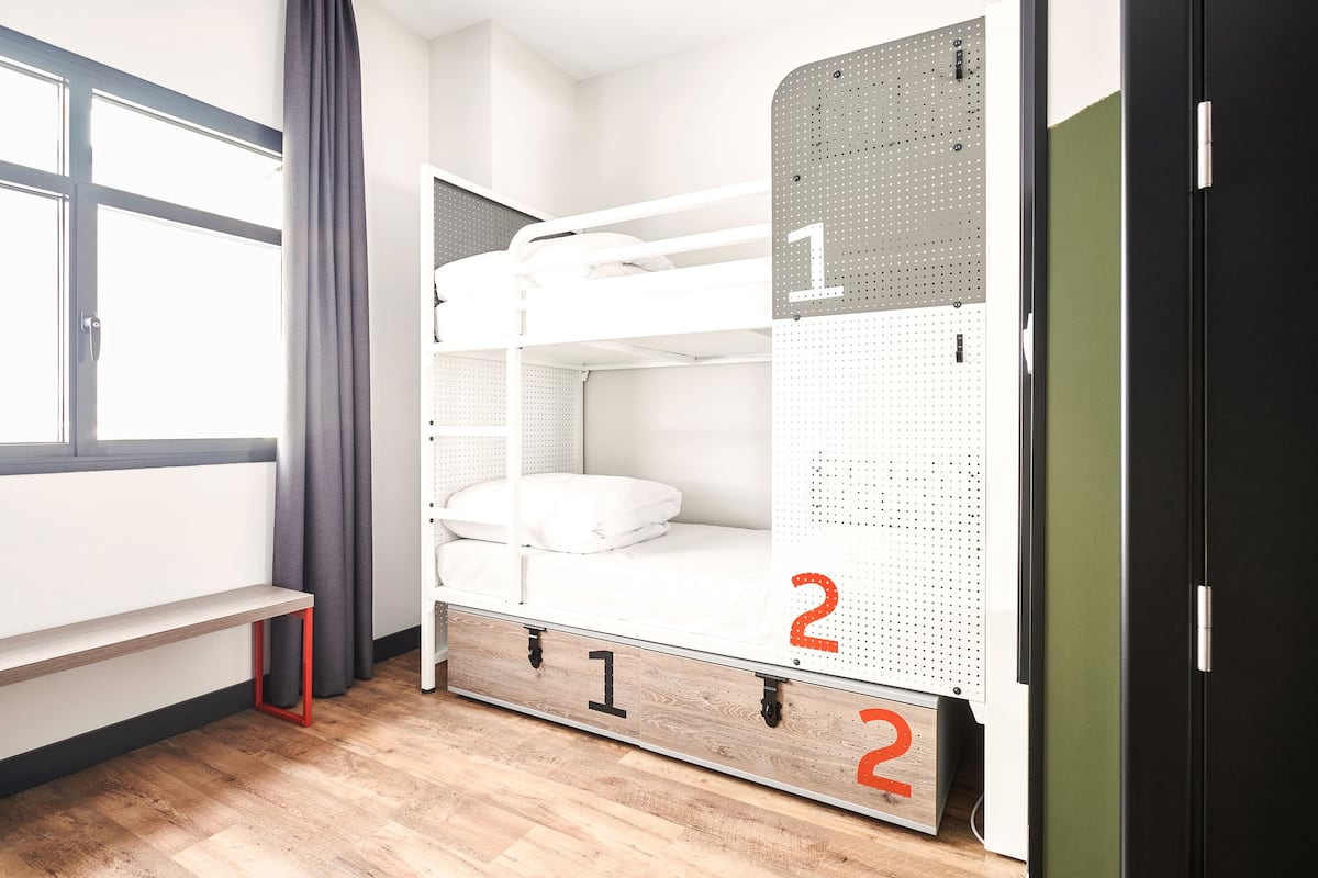 Una cama litera de dos niveles, un banco y una puerta.