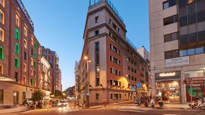 Un edificio de varios pisos con una entrada en esquina, un paso de peatones y una tienda con un letrero.