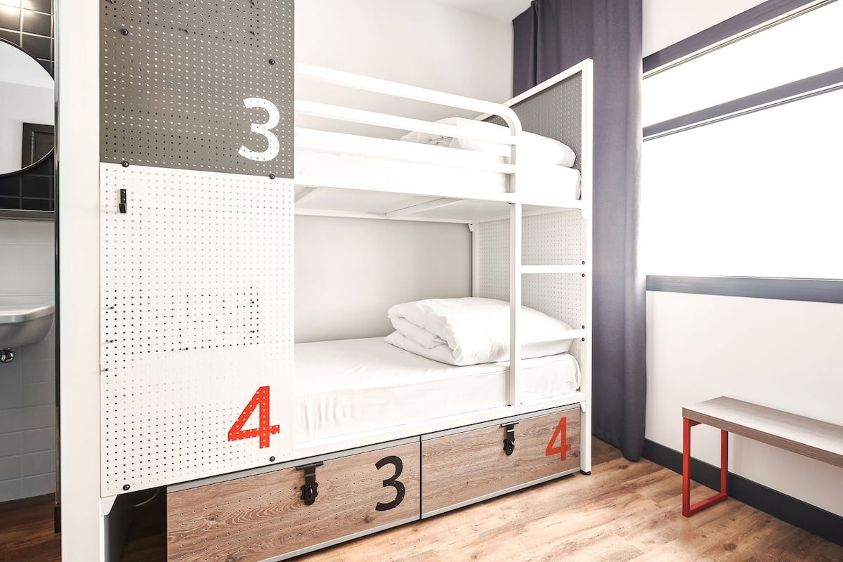 Una cama litera con los números 3 y 4, cajones de madera y un banco.