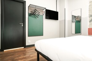 A modern hotel room with a wooden floor, a bed with white bedding, a black door, a wall-mounted TV, and a green abstract painting. - Generator Madrid (Madrid)