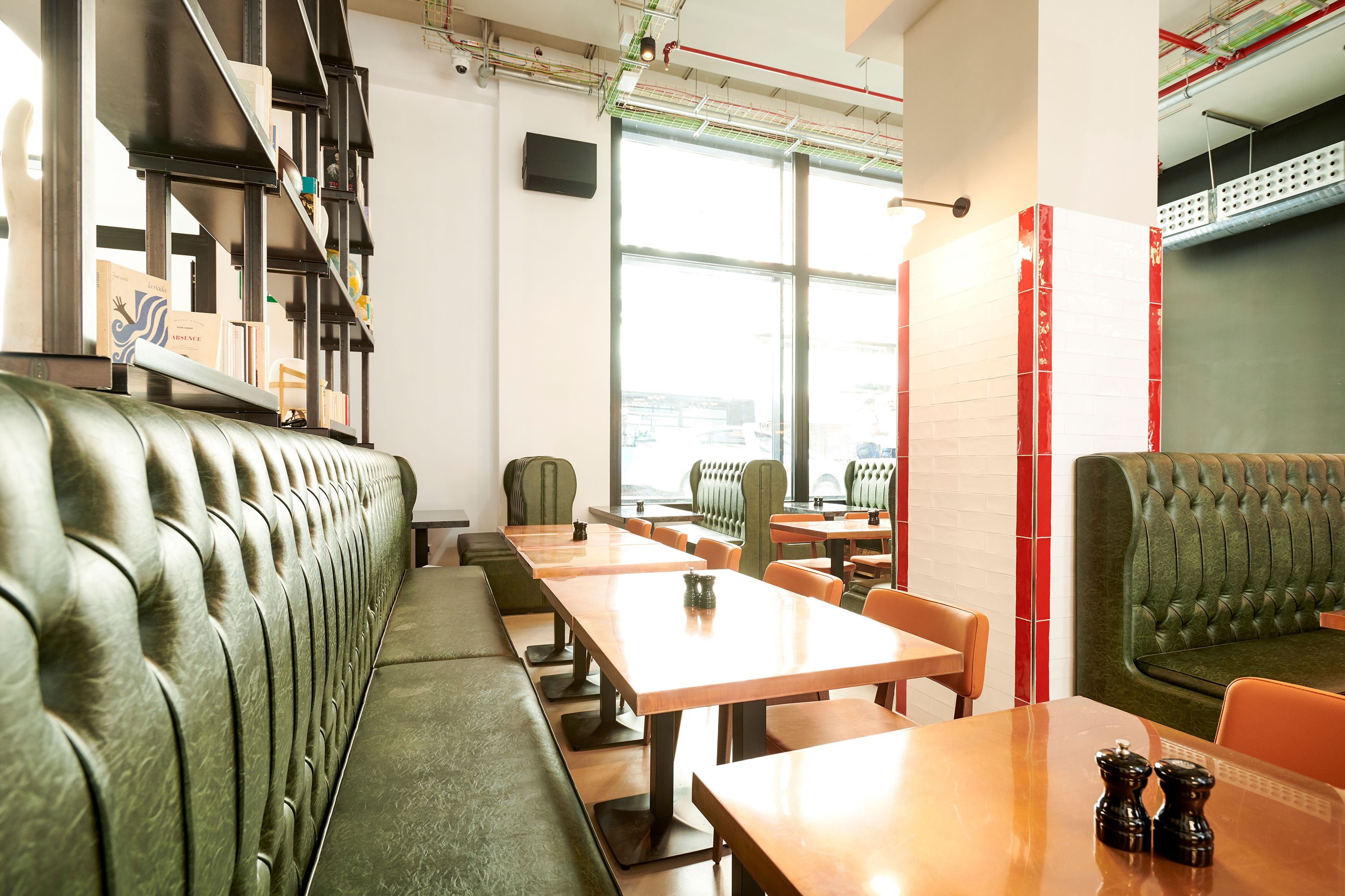 A modern restaurant with green upholstered booths, wooden tables, and a large window offering a view of the city.